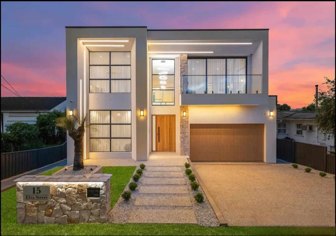 Two-storey contemporary home with stone cladding, large glazing and dramatic dusk lighting.