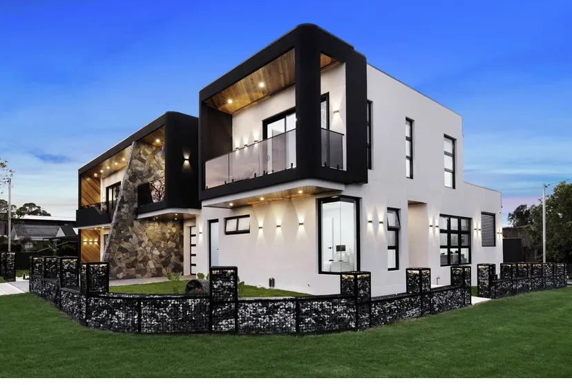 Contemporary duplex with cantilevered black-framed volumes, stone accent wall and laser-cut boundary fence — photographed on completion.
